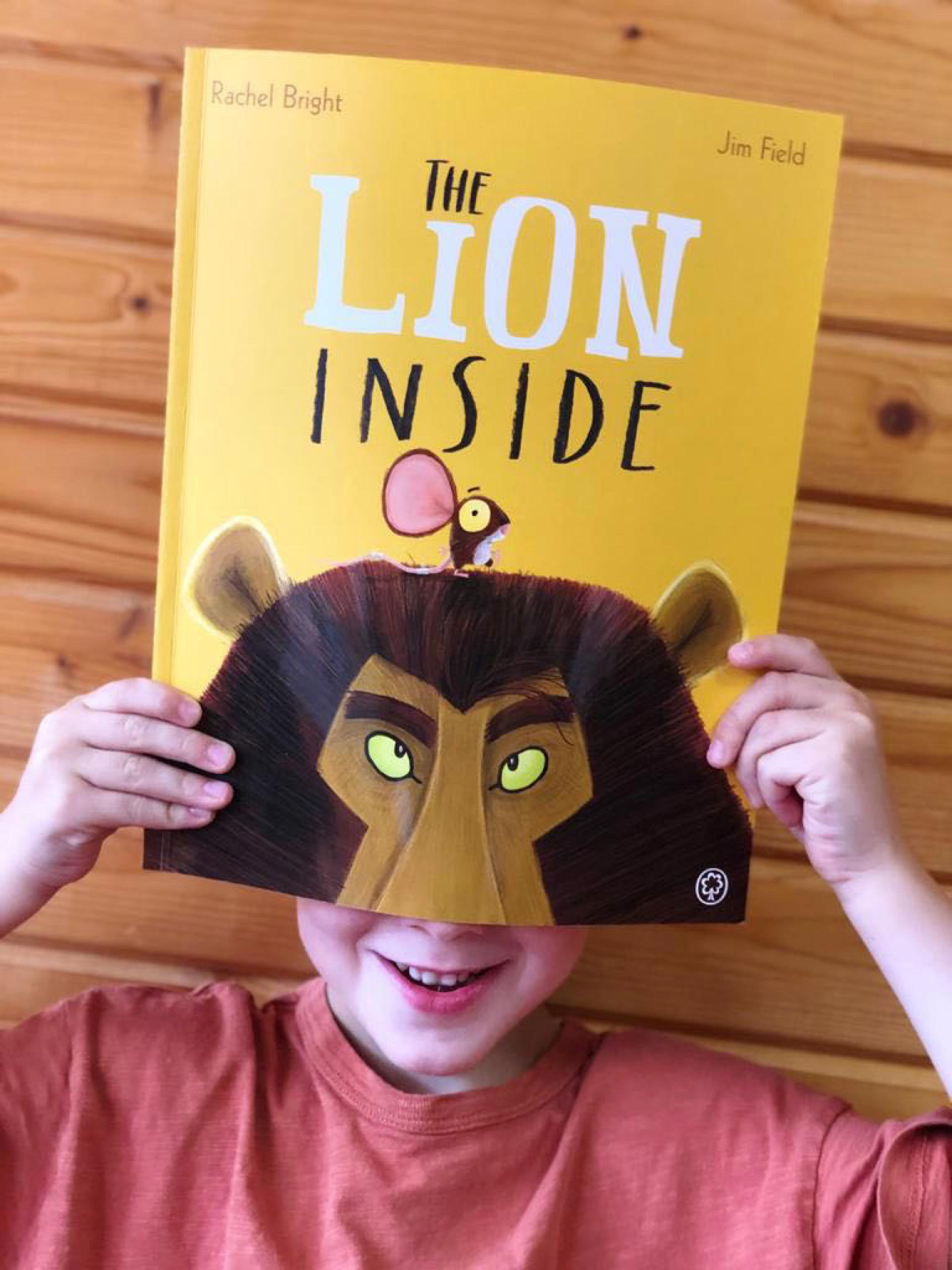 A child holds a book with a lion on the cover in front of his face