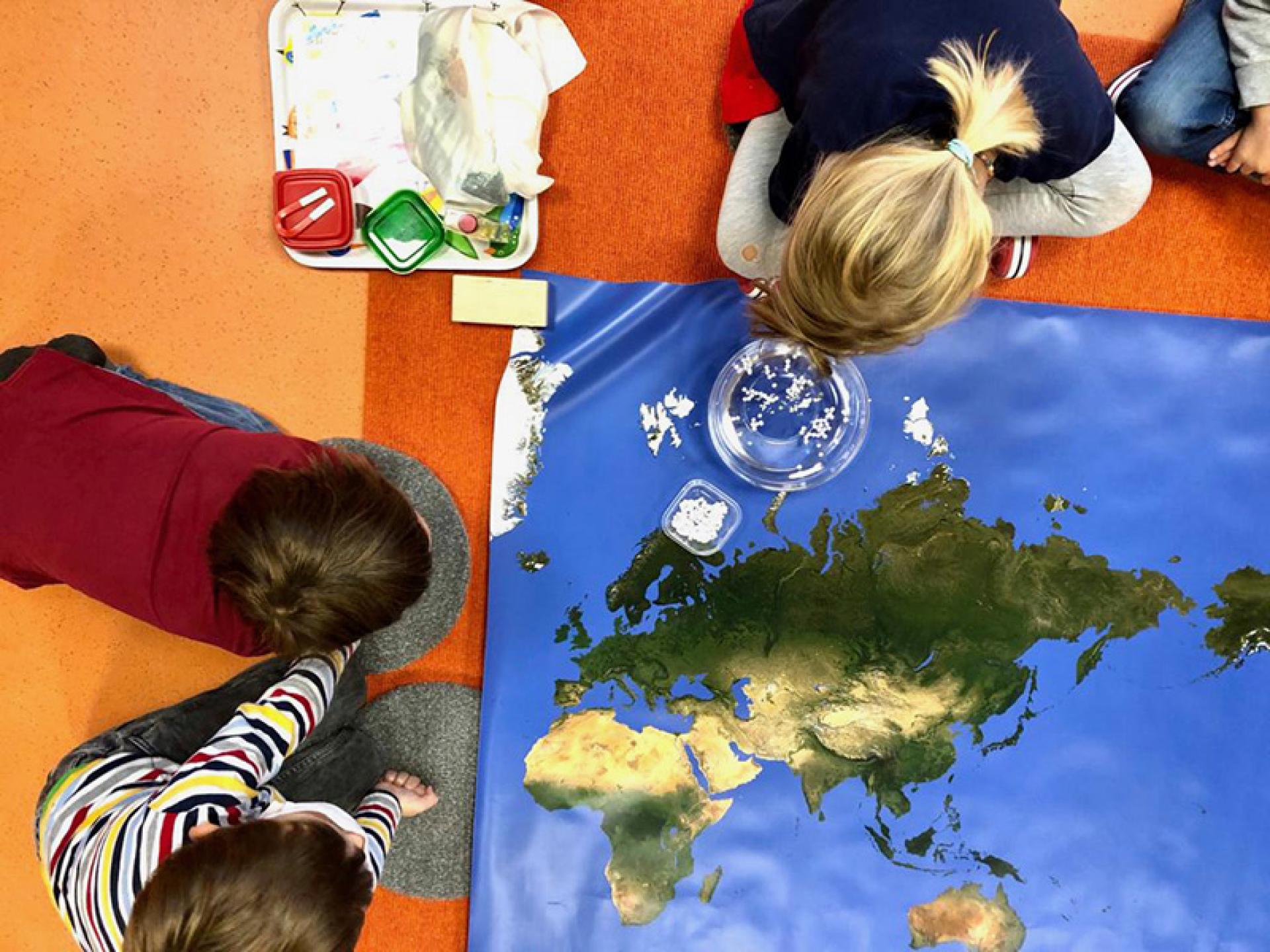 Children play on the floor with a world map and explore different countries and continents